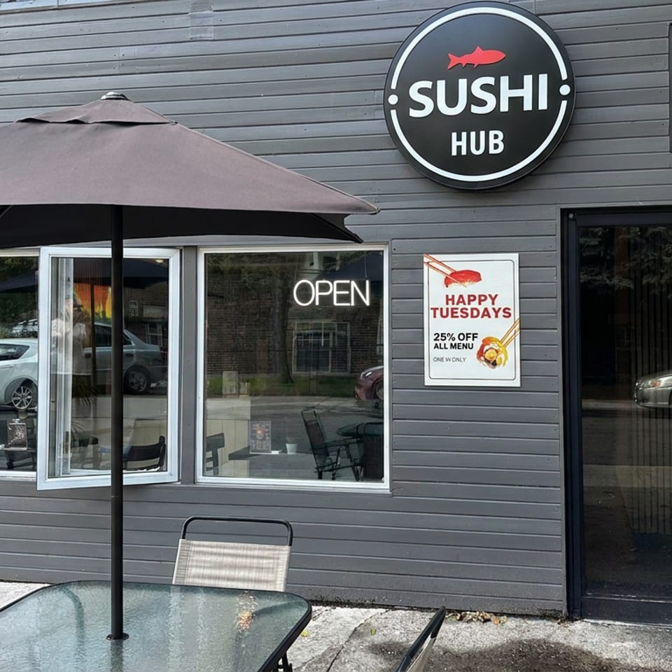 Sushi Hub restaurant exterior with outdoor seating, umbrella, open sign, and promotional Tuesday discount posters.