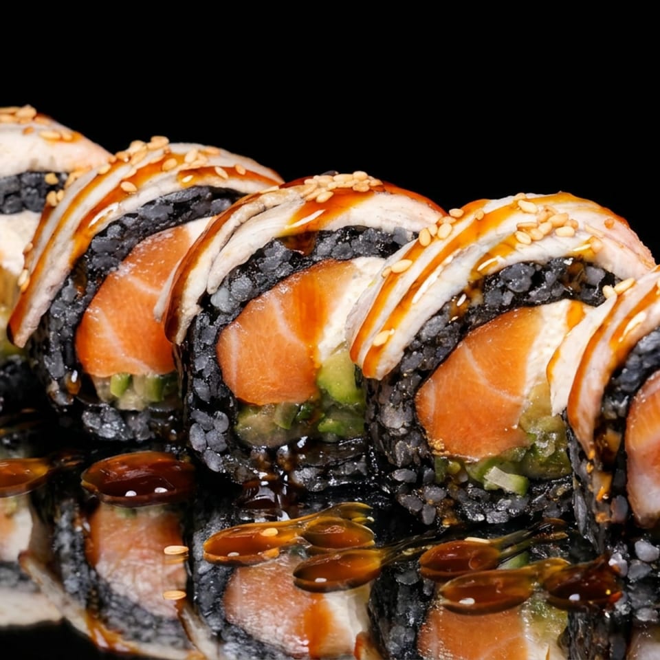 Sushi roll slices with black rice, salmon, avocado, creamy topping, sesame seeds, and teriyaki sauce on a reflective black surface.