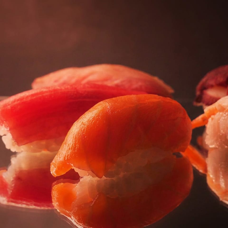 Close-up of assorted sushi nigiri, including salmon, tuna, and shrimp, arranged on a dark surface under warm lighting.